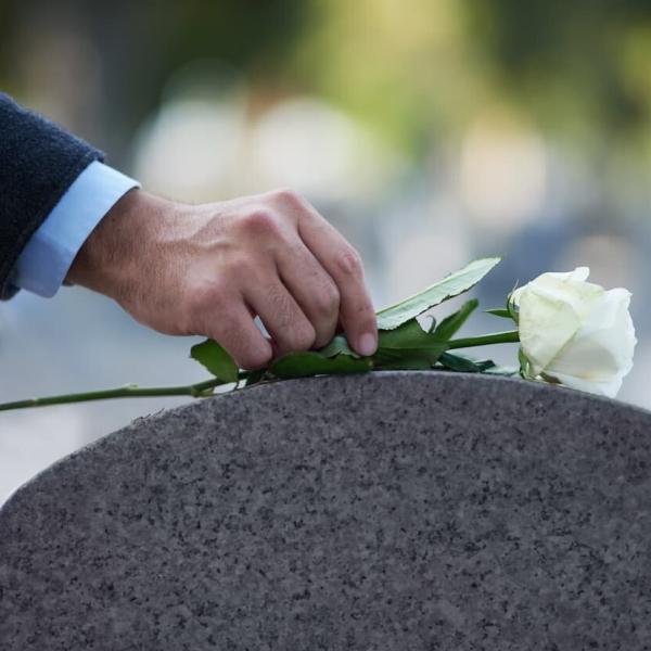 man placing a flower on gravestone