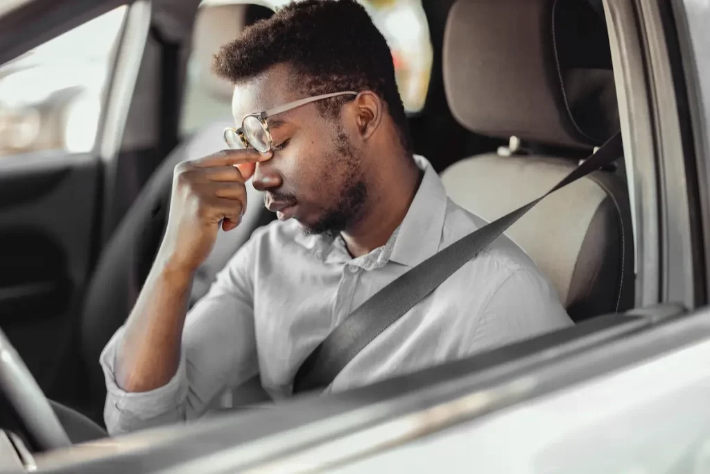 a drowsy driver rubs his eyes